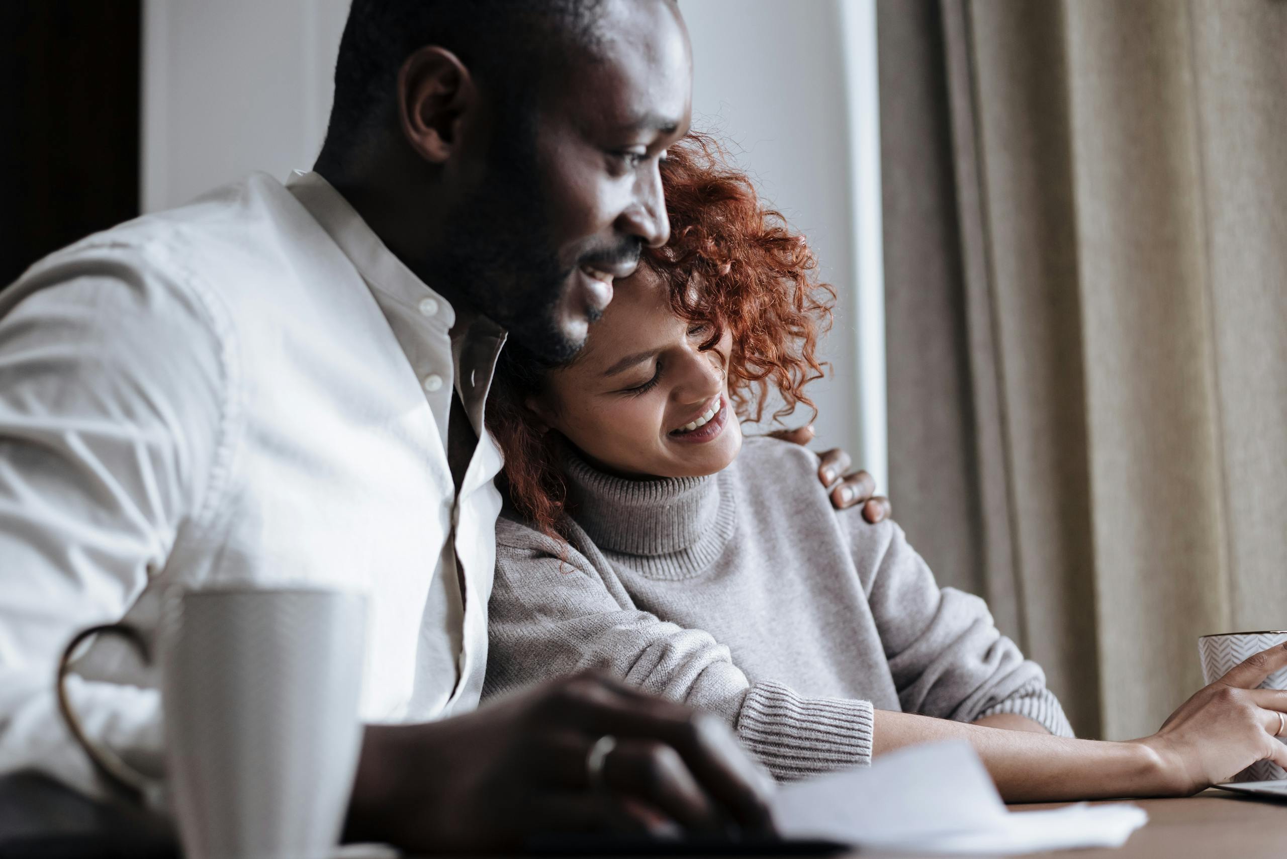 Smiling couple shares a warm moment over coffee in a cozy home setting.